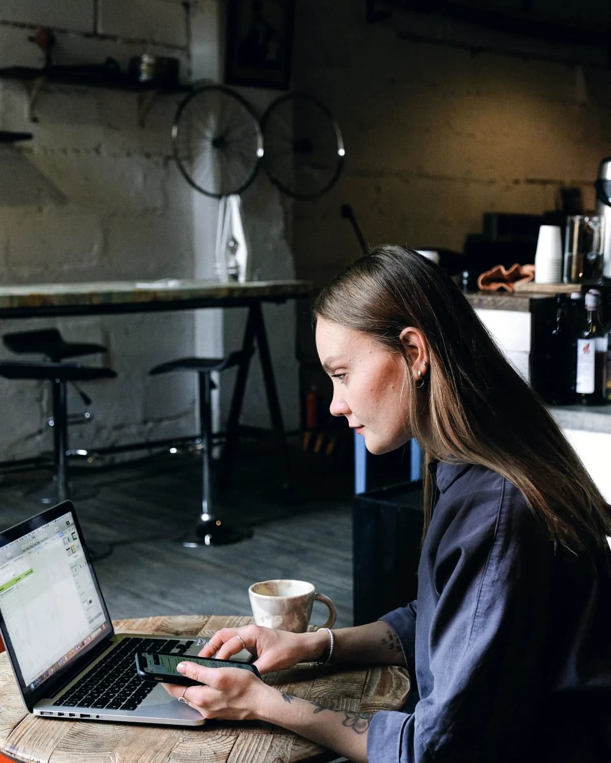 Woman working on a laptop and phone at a café table